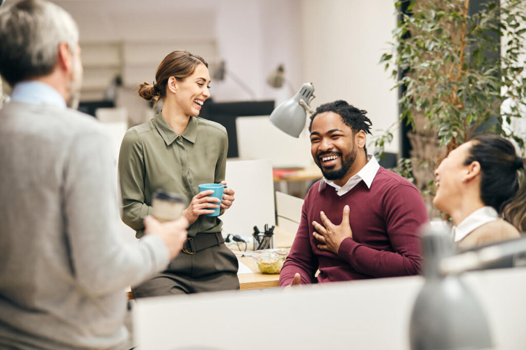 Vier Mitarbeiter reden und lachen im Büro, ein Zeichen einer guten Unternehmenskultur