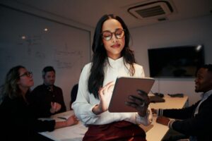 Geschäftsfrau, die Tablet benutzt und vor ihrem Team am Schreibtisch im Besprechungsraum steht
