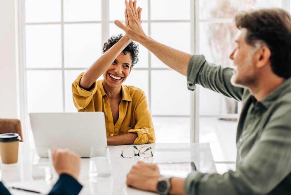 Zwei lächelnde Kollegen geben sich High Five in Büro