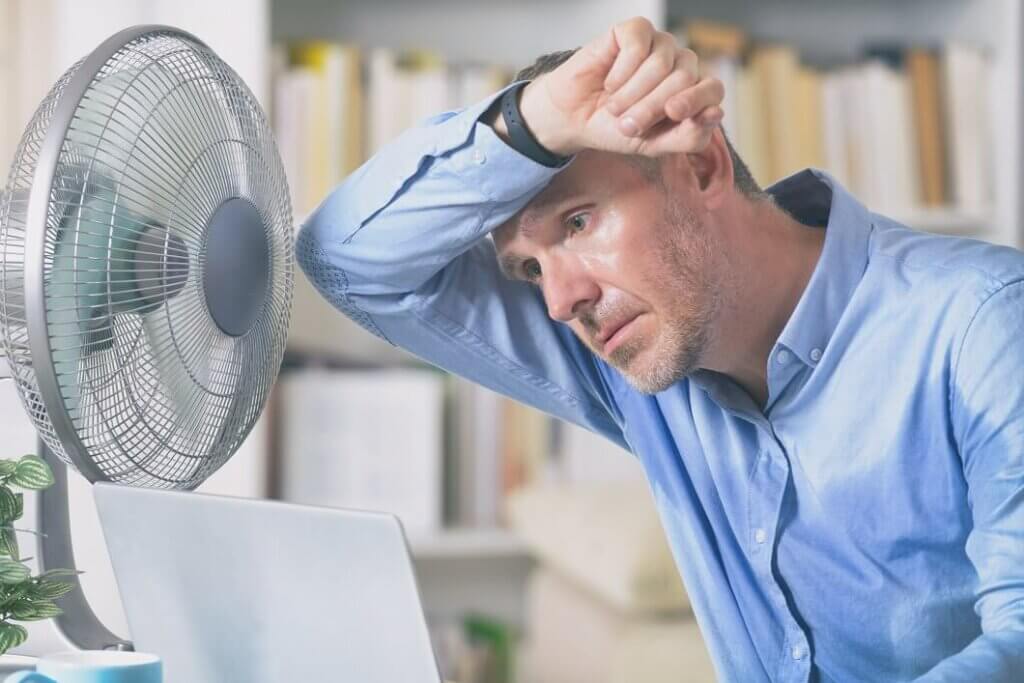 Mann sitzt schwitzend im Büro vor Ventilator