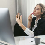 Müde faule Büroangestellte am Arbeitsplatz. Langweilige Arbeit im Büro. Mädchen malt Lippen am Arbeitsplatz