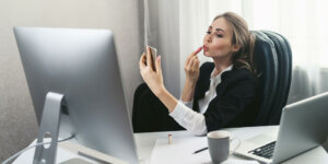 Müde faule Büroangestellte am Arbeitsplatz. Langweilige Arbeit im Büro. Mädchen malt Lippen am Arbeitsplatz