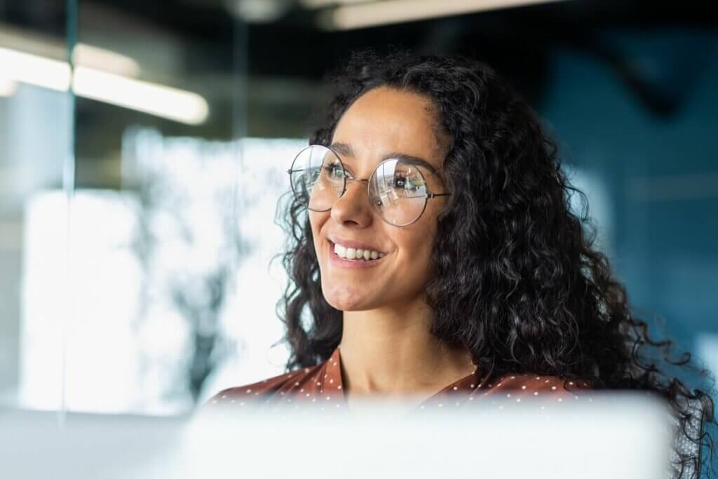 Lächelnde Frau mit Brille vor Laptop denkt über ihren Traumjob nach