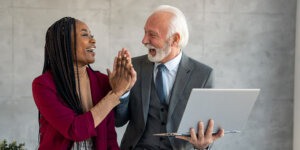Frau und Mann aus zwei verschiedenen Generationen geben sich High Five am Arbeitsplatz
