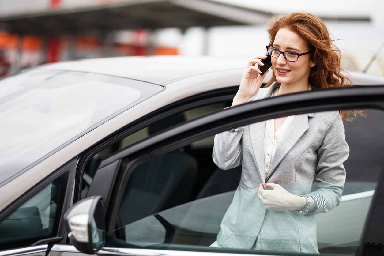 Junge Geschäftsfrau steigt telefonierend in Firmenauto ein