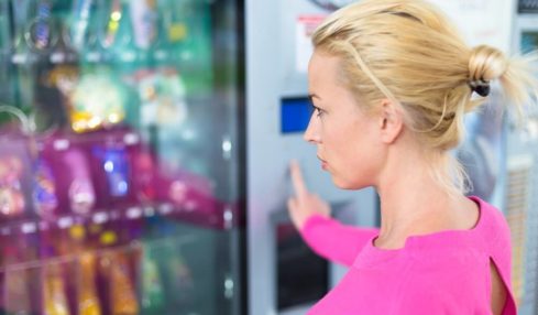Eine blonde Automatenfachfrau Azubine vor einem Automat.