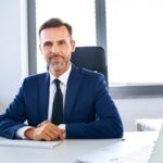 Lächelnder Beamter im mittleren Bankdienst im Anzug am Schreibtisch