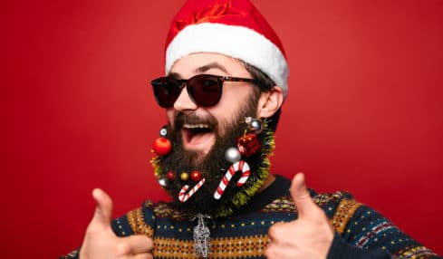 Gut gelaunter Mann mit Nikolausmütze und Sonnenbrille macht thumbs up auf Weihnachtsfeier