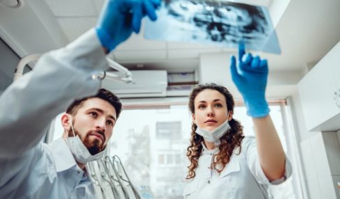 Eine Zahnmedizinische Fachangestelltin hilft einem männlichen Kollegen.