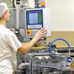 Süßwarentechnologe bedient eine Maschnine und trägt ein Haarnetz.