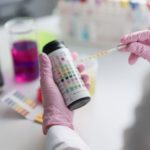 Eine Lacklaborantin mit pinken Gummihandschuhenhält einen Lackmus-Teststreifen in den Händen.