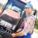 Ein Landmaschinenmechaniker mit blauer Mütze beim Reparieren eines Traktors