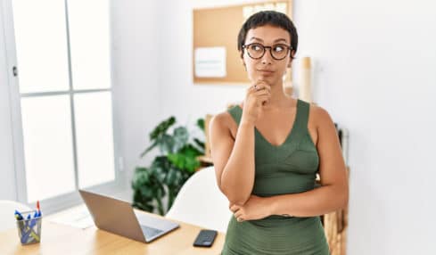 Eine kurzhaarige Frau mit einem engnaliegenden, olivengrünen Kleid denkt über ihr Sommer Büro Outfit nach