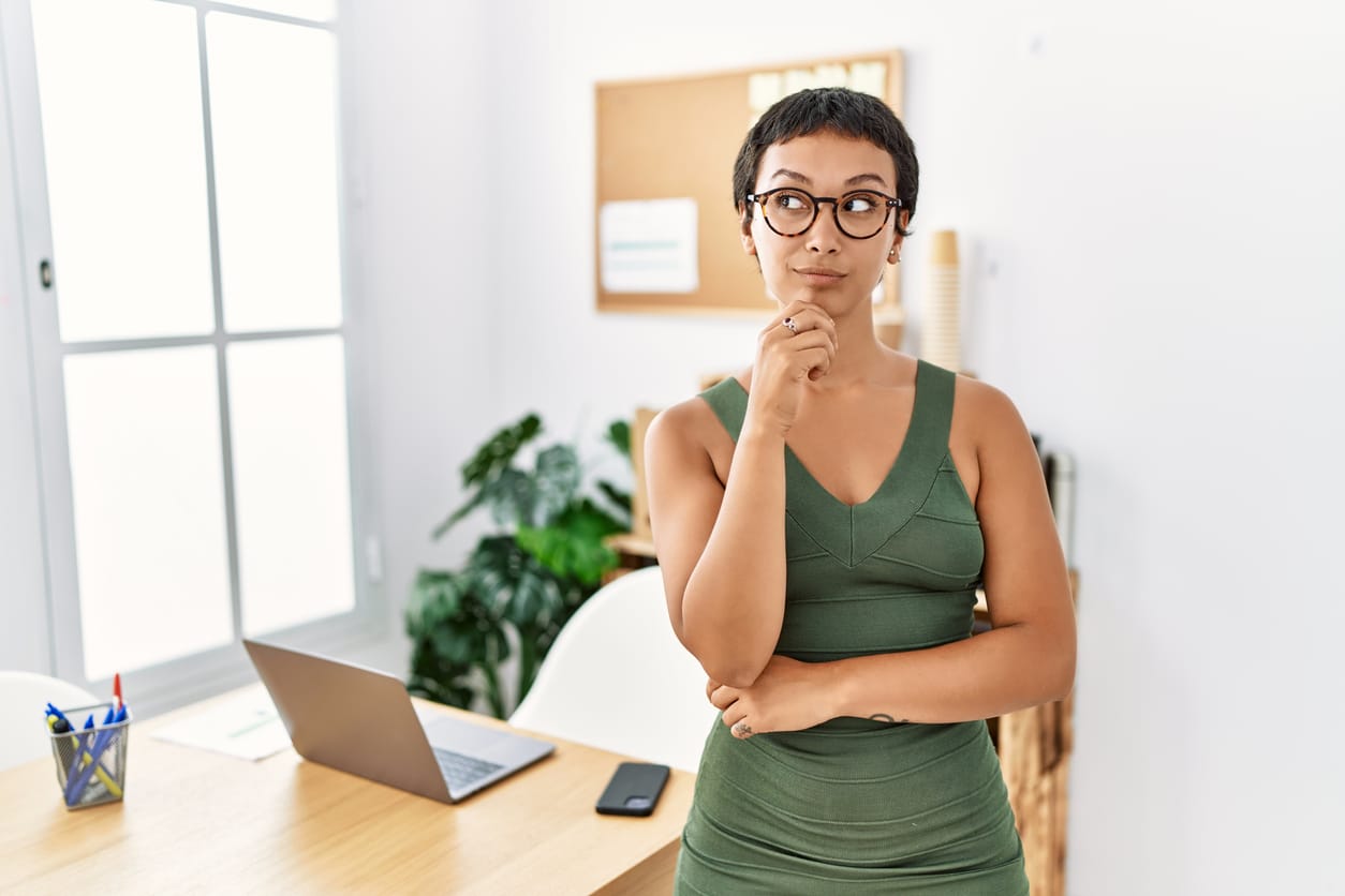 Eine kurzhaarige Frau mit einem engnaliegenden, olivengrünen Kleid denkt über ihr Sommer Büro Outfit nach