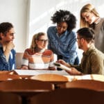 Fünf Arbeitskollegen unterhalten sich am Tisch über Berufe in der Erwachsenenbildung
