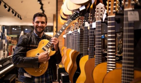 Ein Azubi der Musikfachhändlre Ausbildung hält eine E-Gitarre in den Händen im Musikgeschäft