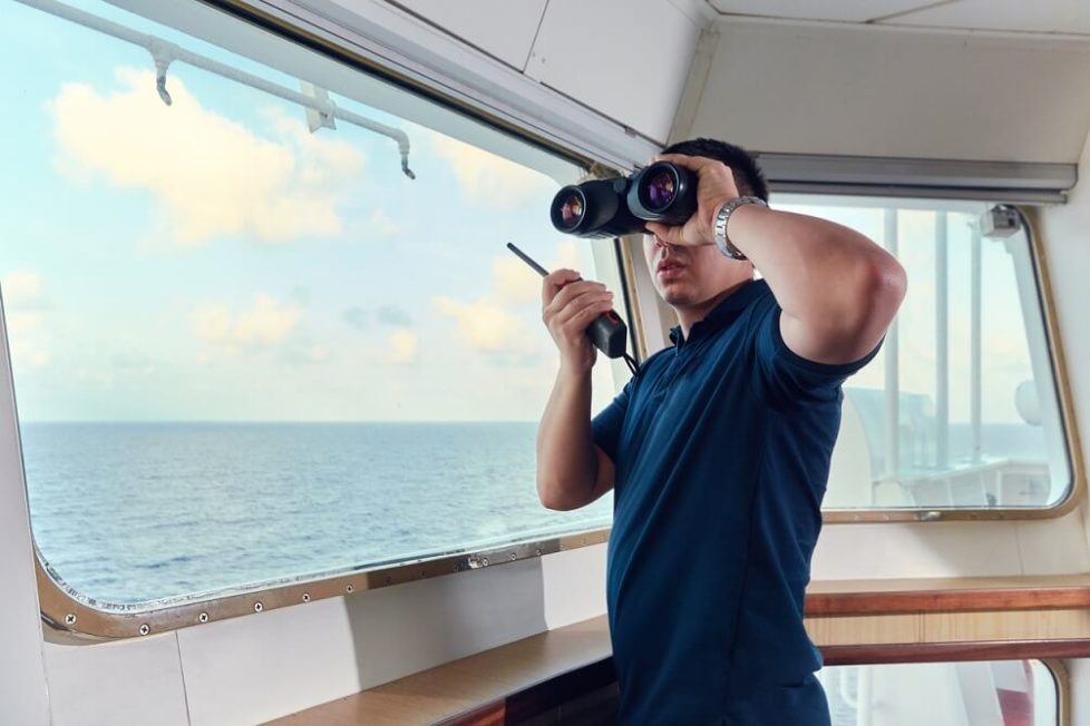 Ein angehender Nautischer Offiziersass mit Fernglas & Walkie-Talkie während der Ausbildung auf dem Schiff