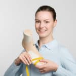 Eine lächelnde Azubine der Orthopaedieschuhmacher-Ausbildung hält einen Schuhleisten in beiden Händen
