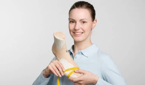 Eine lächelnde Azubine der Orthopaedieschuhmacher-Ausbildung hält einen Schuhleisten in beiden Händen
