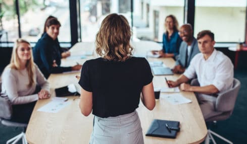 Eine Business-Frau überzeugt bei einem Meeting ihre Kollegen durch ihr sicheres Auftreten.