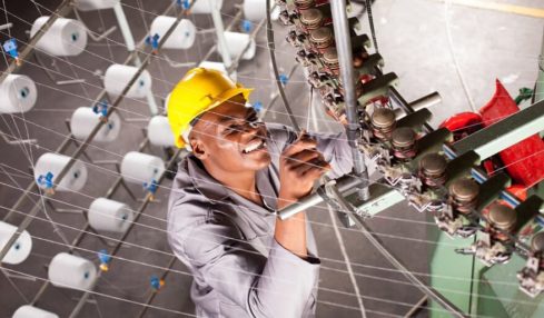 Ein lächelnder, angehender Textillaborant beim Betätigen einer Maschine in der Ausbildung