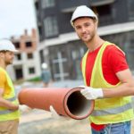 2 angehende Tiefbaufacharbeiter in der Ausbildung halten ein großes Plastikrohr auf der Baustelle