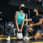 Ein muskulöser angehender Sport- und Fitnesskaufmann hilft einer Fitness-Center-Besucherin in der Ausbildung