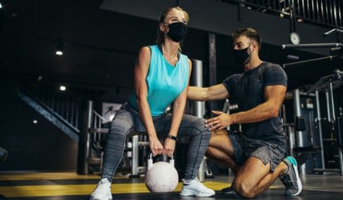 Ein muskulöser angehender Sport- und Fitnesskaufmann hilft einer Fitness-Center-Besucherin in der Ausbildung