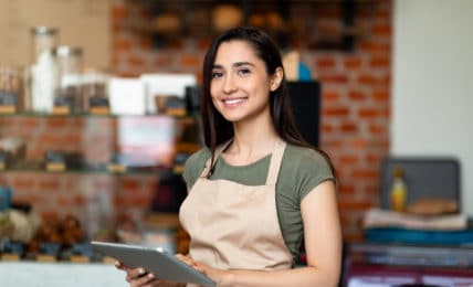 Junge Mitarbeiterin im Café mit Laptop freut sich über neue Verdienstgrenze im Minijob