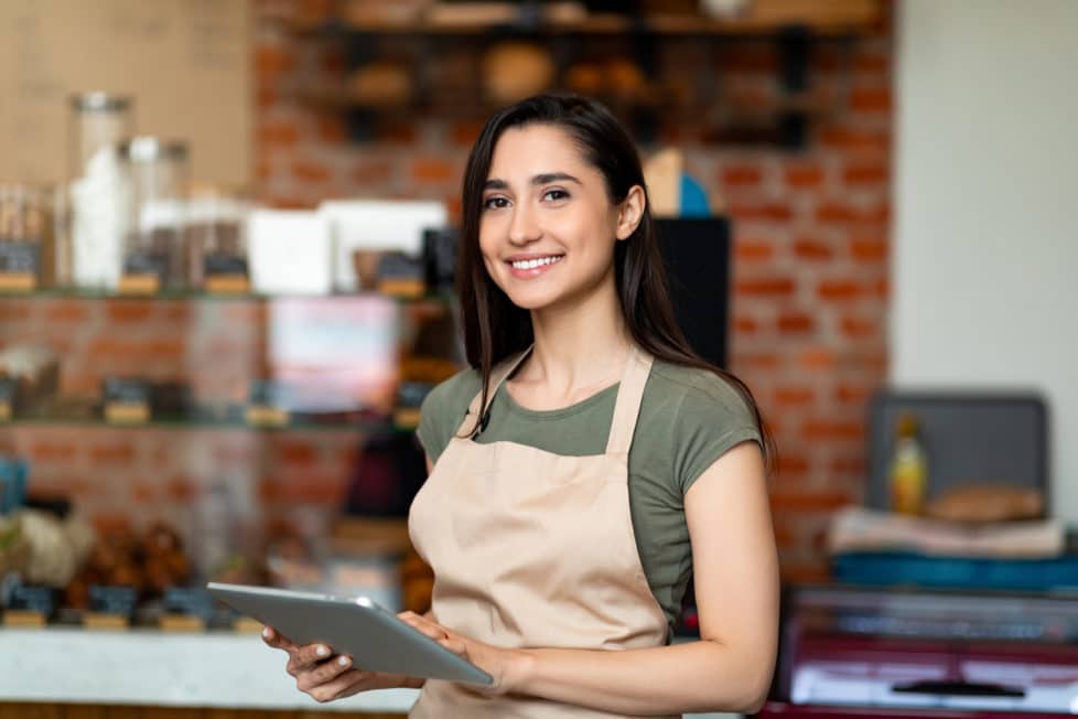 Junge Mitarbeiterin im Café mit Laptop freut sich über neue Verdienstgrenze im Minijob