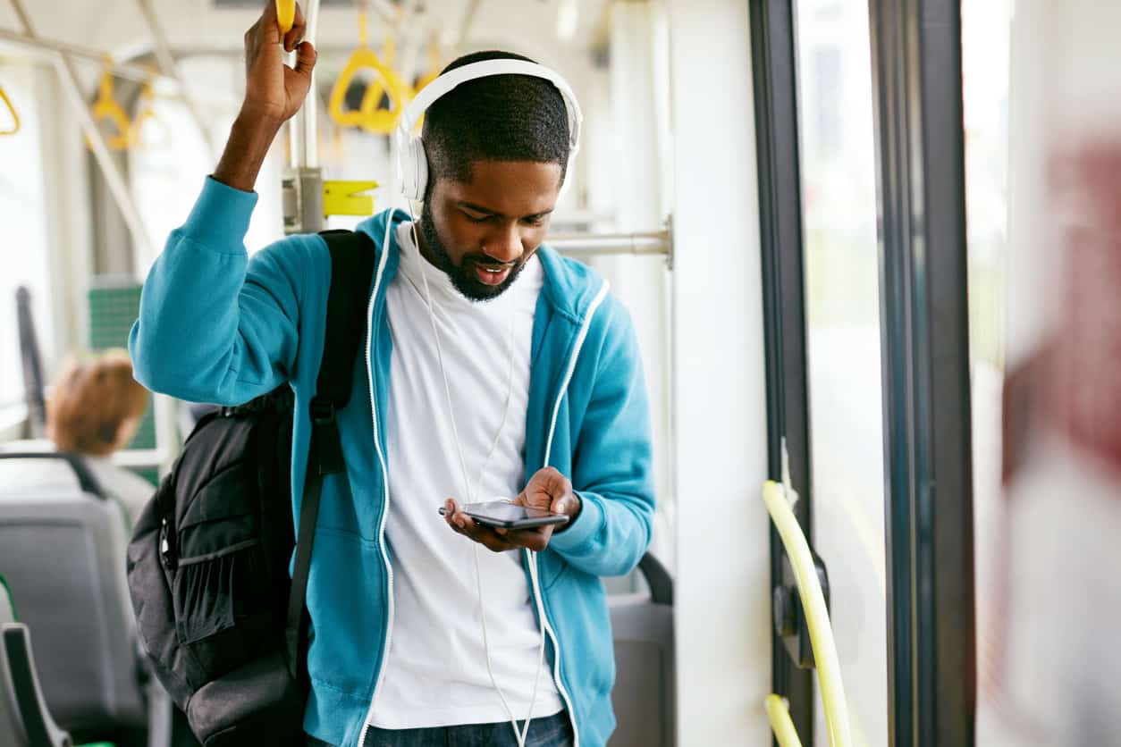 Junger Mann in U-Bahn mit Kopfhörern und Smartphone in der Hand