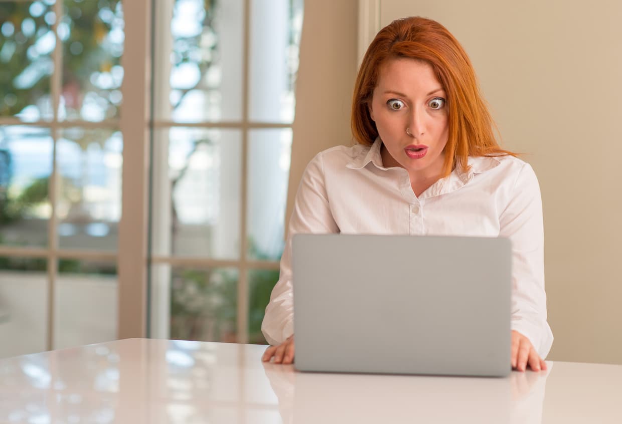 Frau liest auf Laptop und reißt extrem überrascht die Augen auf