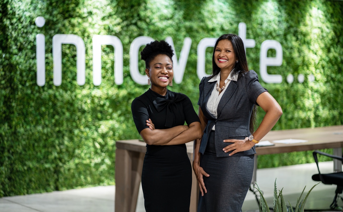 Zwei lächelnde Geschäftsfrauen vor grüner Wand mit Aufschrift "innovate""