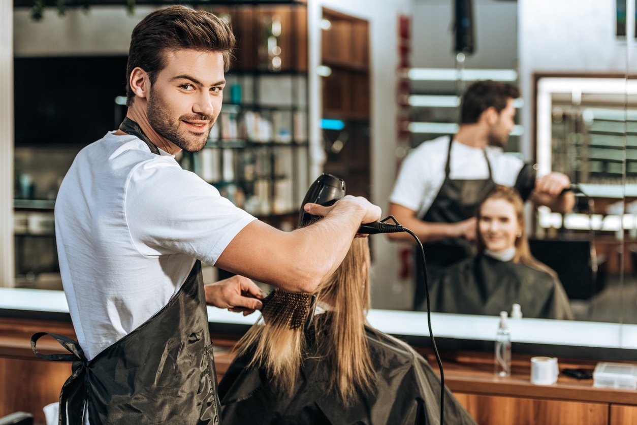 Männlicher Friseur föhnt Kundin im Salon die Haare