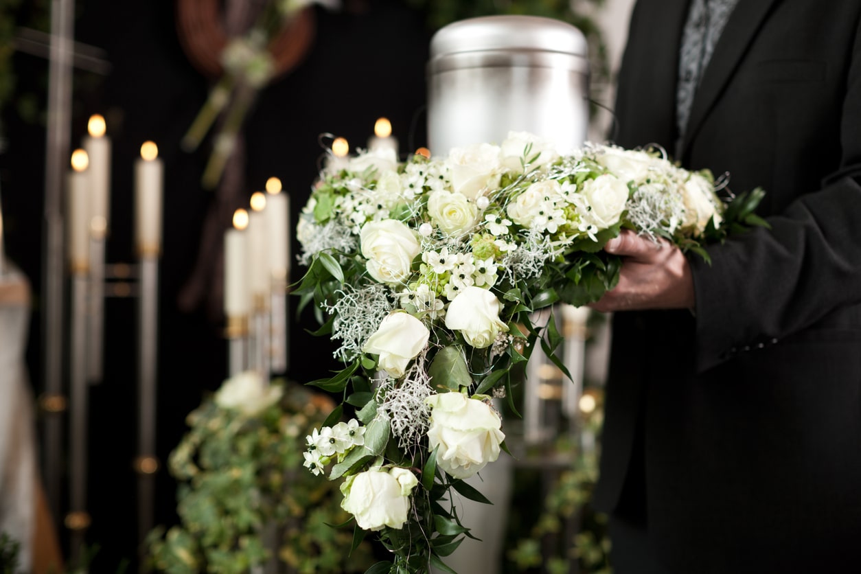 Bestatter präsentiert Blumenschmuck vor Urne