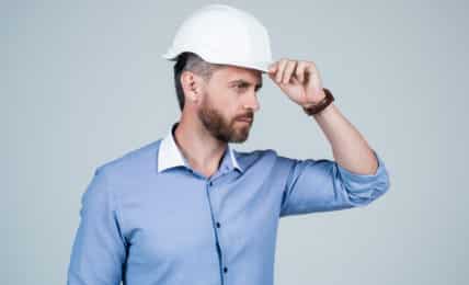 Arbeitnehmer mit Schutzhelm blickt nach rechts und hält Hand am Helm