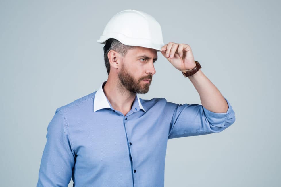 Arbeitnehmer mit Schutzhelm blickt nach rechts und hält Hand am Helm