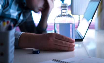 Alkohol am Arbeitsplatz Mann sitzt mit Wodkaflasche in der Hand vor Laptop