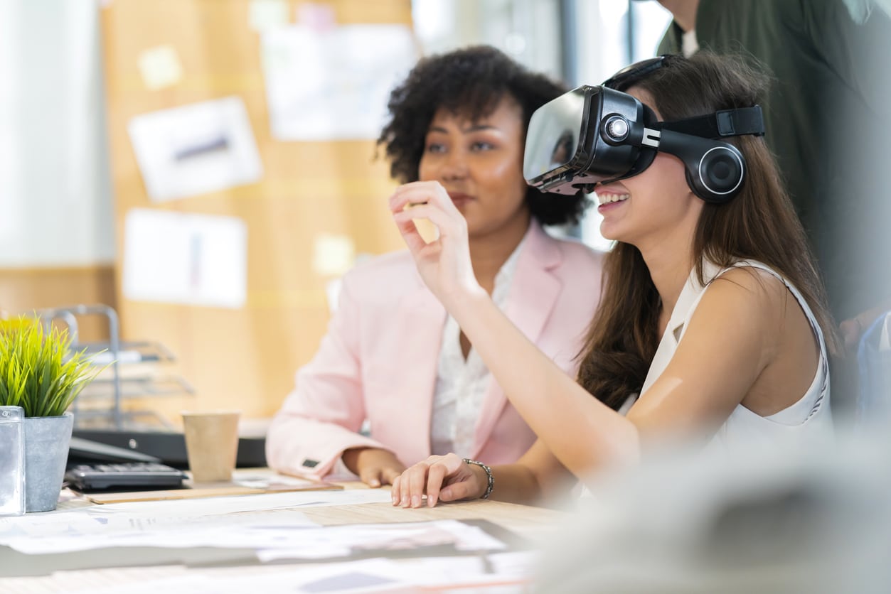 Junge Frau der Generation Z im Büro trägt VR-Brille am Schreibtisch
