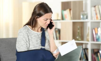 Frau mit verletztem Arm diskutiert am Telefon über Lohnfortzahlung im Krankheitsfall