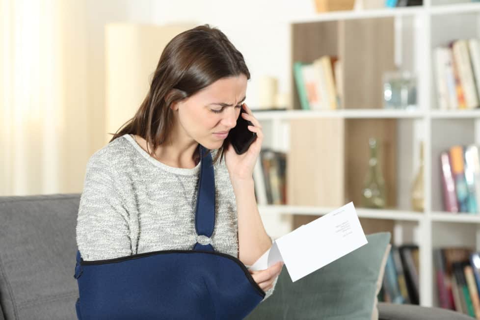 Frau mit verletztem Arm diskutiert am Telefon über Lohnfortzahlung im Krankheitsfall