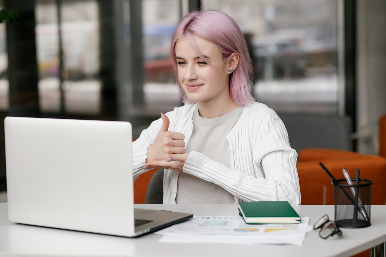 Junge Frau vor Laptop zeigt nonverbal Daumen hoch