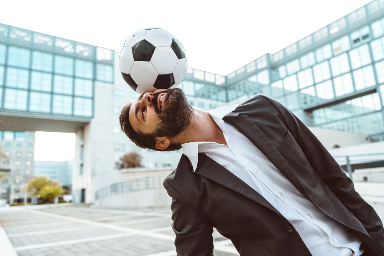 Berufe mit Sport - Geschäftsmann im Anzug kickt Ball mit Kopf