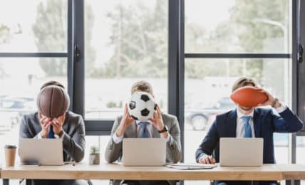 Berufe mit Sport - 3 Geschäftsmänner vor Laptops mit Bällen vor dem Gesicht