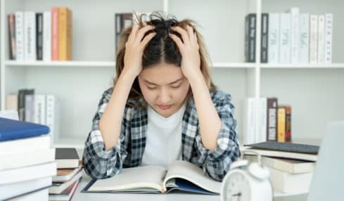 Regelstudienzeit - junge Studentin lernt verzweifelt über Büchern mit Wecker auf dem Tisch