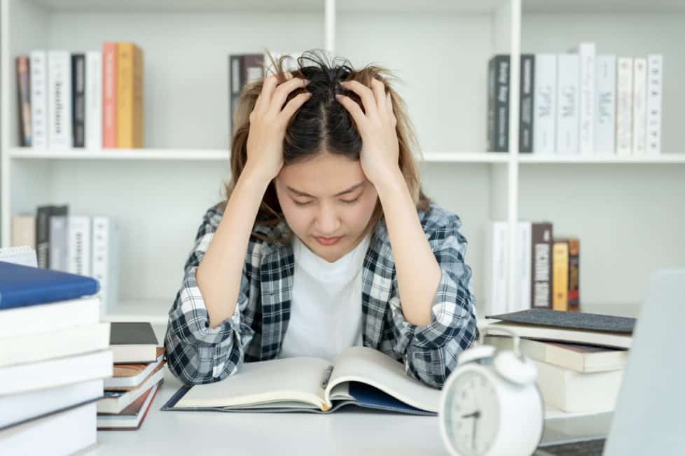 Regelstudienzeit - junge Studentin lernt verzweifelt über Büchern mit Wecker auf dem Tisch