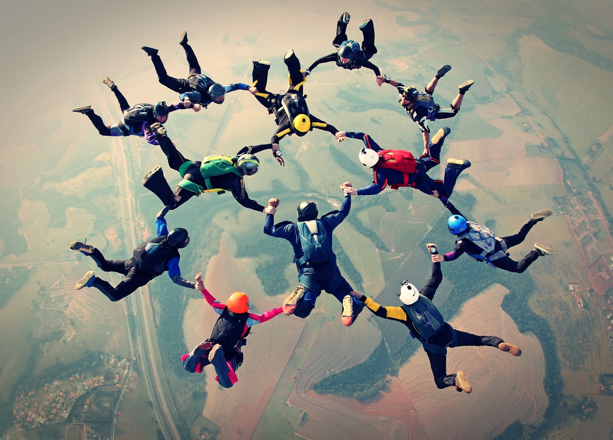12 Menschen gemeinsam Hand in Hand beim Fallschirmsprung - Teamfähigkeit