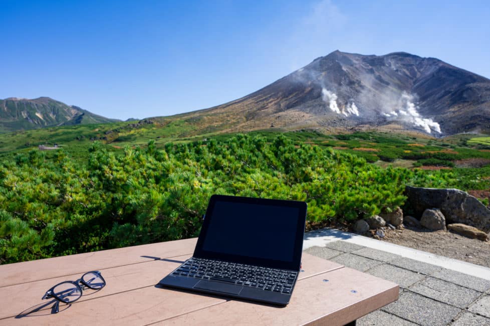 Laptop auf Schreibtisch vor Vulkan - Homeoffice im Ausland