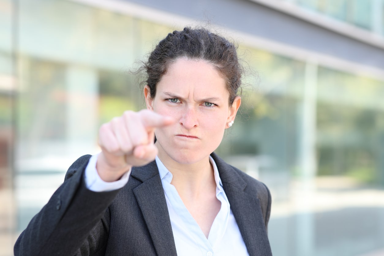 Wütende Mitarbeiterin deutet mit Zeigefinger in Kamera - Kritik am Chef