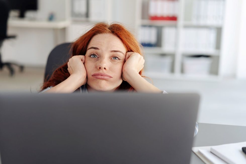 Frau guckt müde über Laptop hinweg - Tipps gegen Müdigkeit im Büro